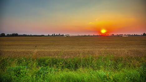 Timelapse-shot-of-combine-harvesters-harvesting-along-a-wheat-field-with-sun-rising-in-the-background-during-morning-time