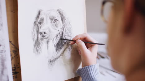 Female-Teenage-Artist-Sitting-At-Easel-Drawing-Picture-Of-Dog-From-Photograph-In-Charcoal