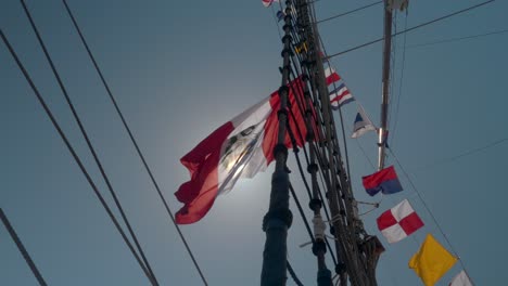 flag waves in breeze high above on colorful tallship mast and rigging