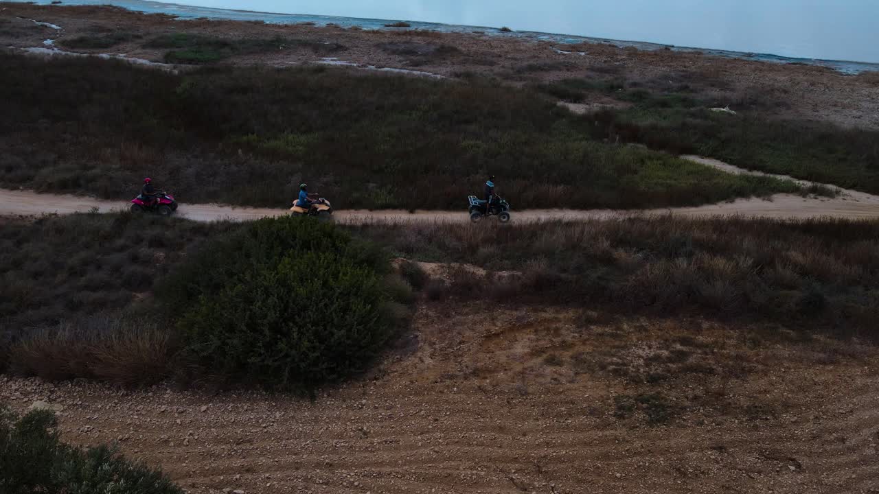 Group of People Riding ATVs on a Dirt Track through Arid Landscape