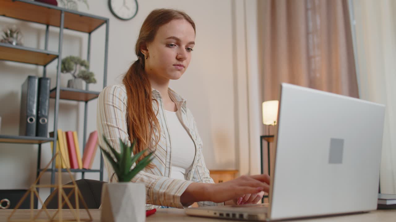 Young woman girl using laptop computer sitting at table working typing on keyboard from home office