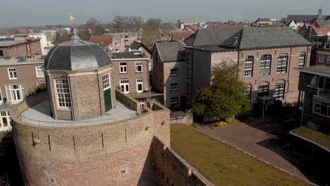 Slow-forwards-aerial-showing-historic-remains-of-Bourgonje-stronghold-tower-and-city-wall-with-golden-wind-ornament,-greenery-roof-and-historic-buildings-in-Zutphen,-The-Netherlands