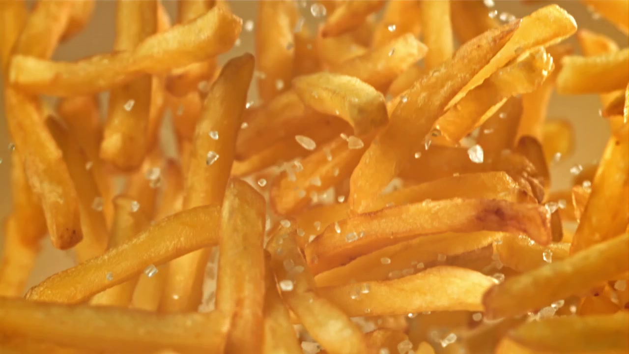 Knusprige goldene Pommes Frites fallen mit Salz in Zeitlupe.