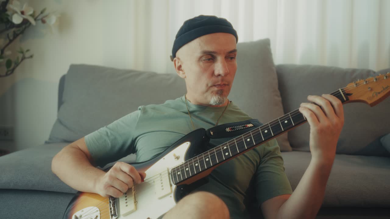 Dospělý muž cvičící na elektrickou kytaru v neformálním domácím prostředí.