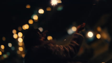 happy woman holding sparklers on rooftop at night playfully waving arms raised celebrating new years eve enjoying independence day celebration with city lights in background