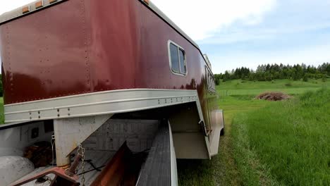 Pickup-truck-pulls-horse-trailer-out-of-meadow-landscape,-back-POV-view