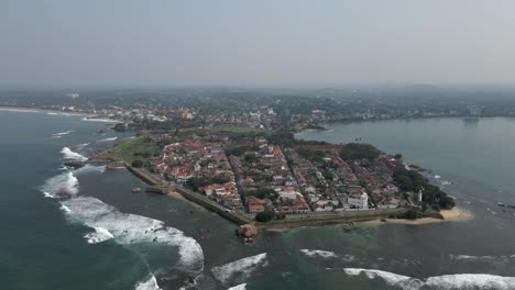 aerial: waves gently break on shore, homes protected by old fort walls