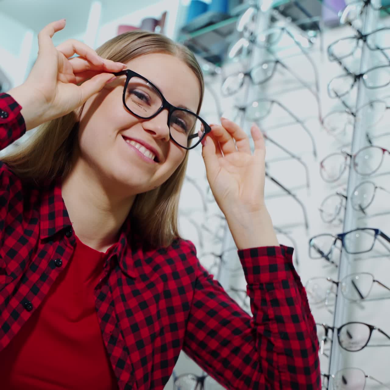 Smiling girl buying eyeglasses in the shop. Attractive young woman trying on new glasses and posing on camera at optics store.
