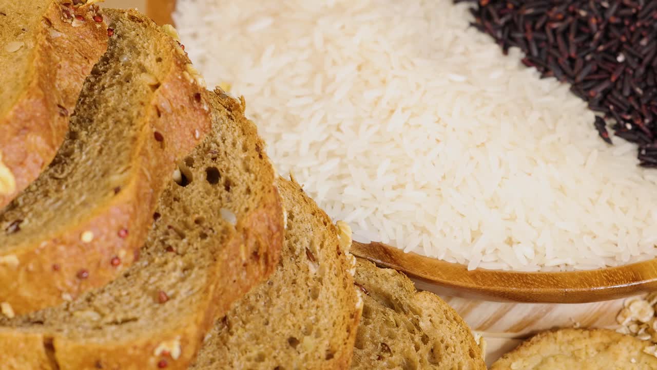 Assorted grains, pasta, and bread on a wooden surface under warm lighting. Close-up shots emphasize texture and variety