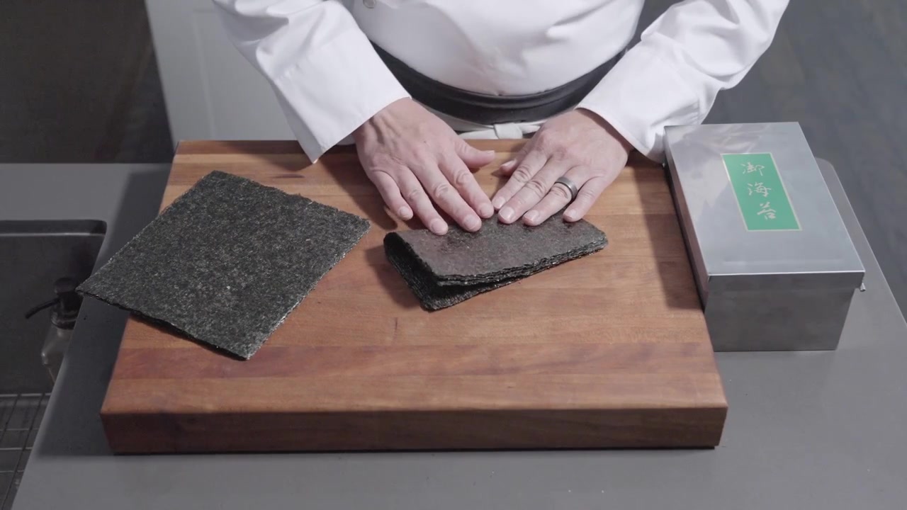 An overhead static shot of a chef entering the scene, carefully folding, cutting, and storing sheets of seaweed. Perfect for culinary and food prep content, showcasing precise kitchen techniques.