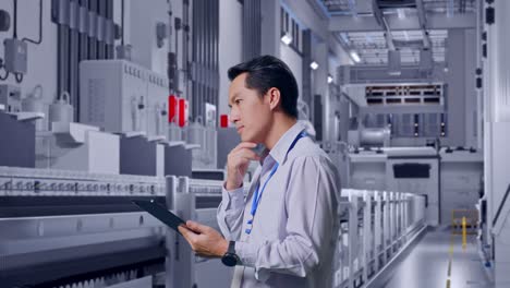 side view of an asian male professional worker at pharmaceutical factory, vaccine production facility, observes by looking up before he come to concentrating on the tablet and keep on checking