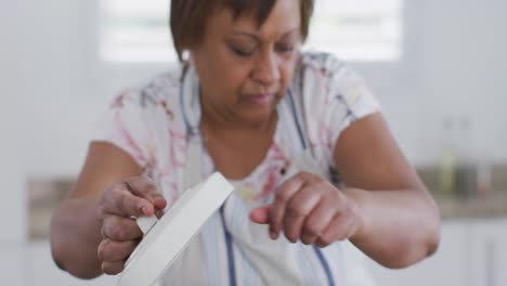 African-american-senior-woman-preparing-food-in-kitchen,-composting-vegetable-waste-and-smiling