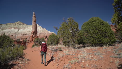 lonely female hiker on hiking trail in desert landscape under red rock spire sandstone formation, slow motion