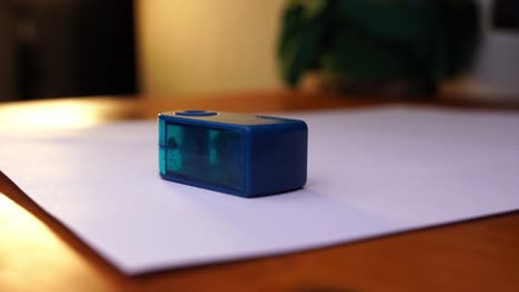 a small, closed sharpener is placed on a piece of paper and taken away again by a hand