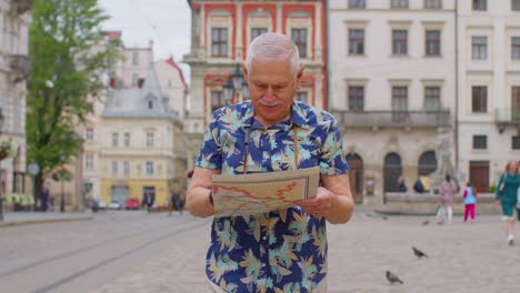 Senior-stylish-tourist-grandfather-man-walking-along-street-looking-for-way-using-paper-map-in-city