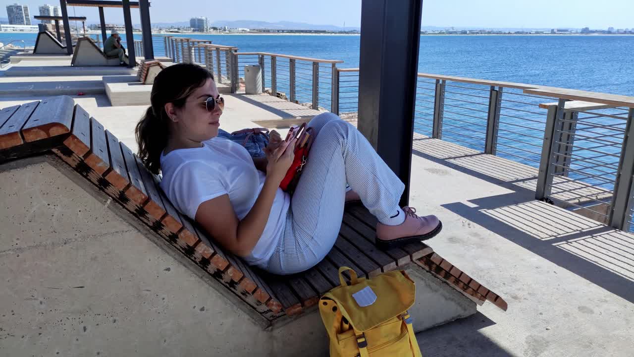 Traveler texting on phone while resting on a modern promenade bench