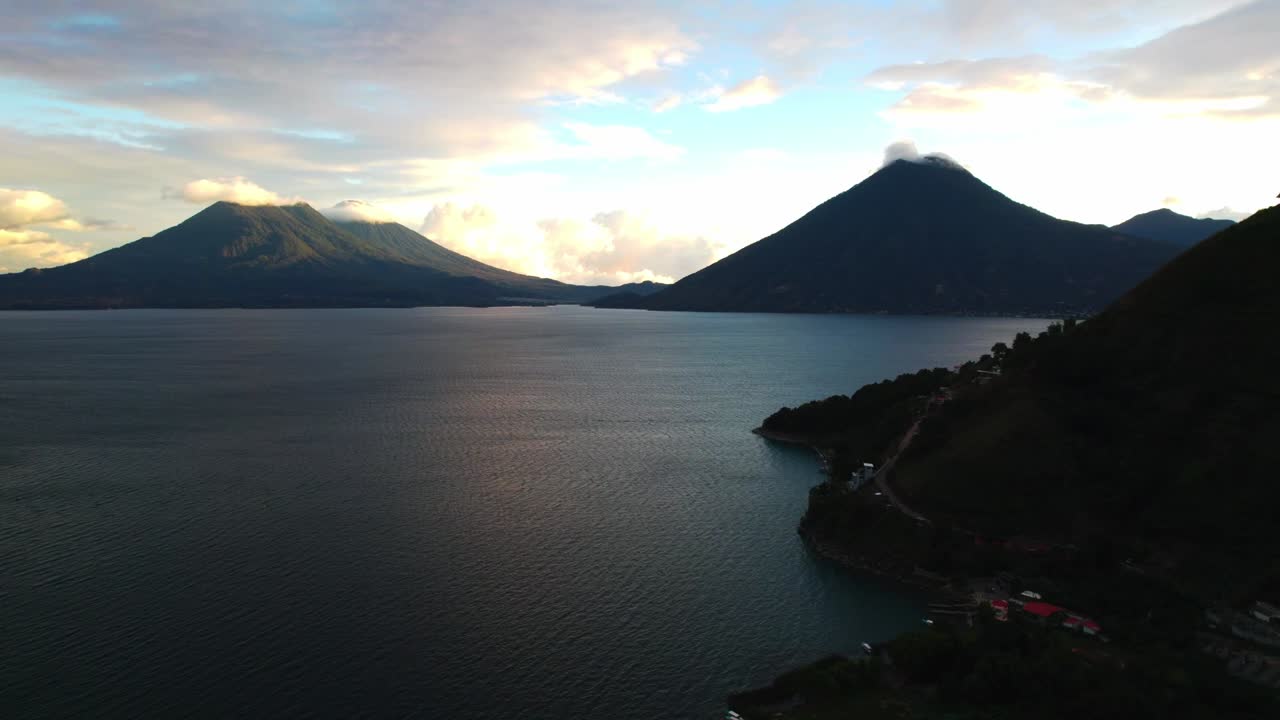 Luftfotozoom ind mod vulkanbjerge, der rejser sig over Lake Atitlan med blødt dagslys og teksturerede skyer