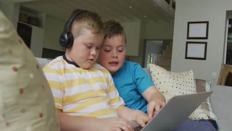 niño caucásico con su hermano sentado en la sala de estar y usando una computadora portátil