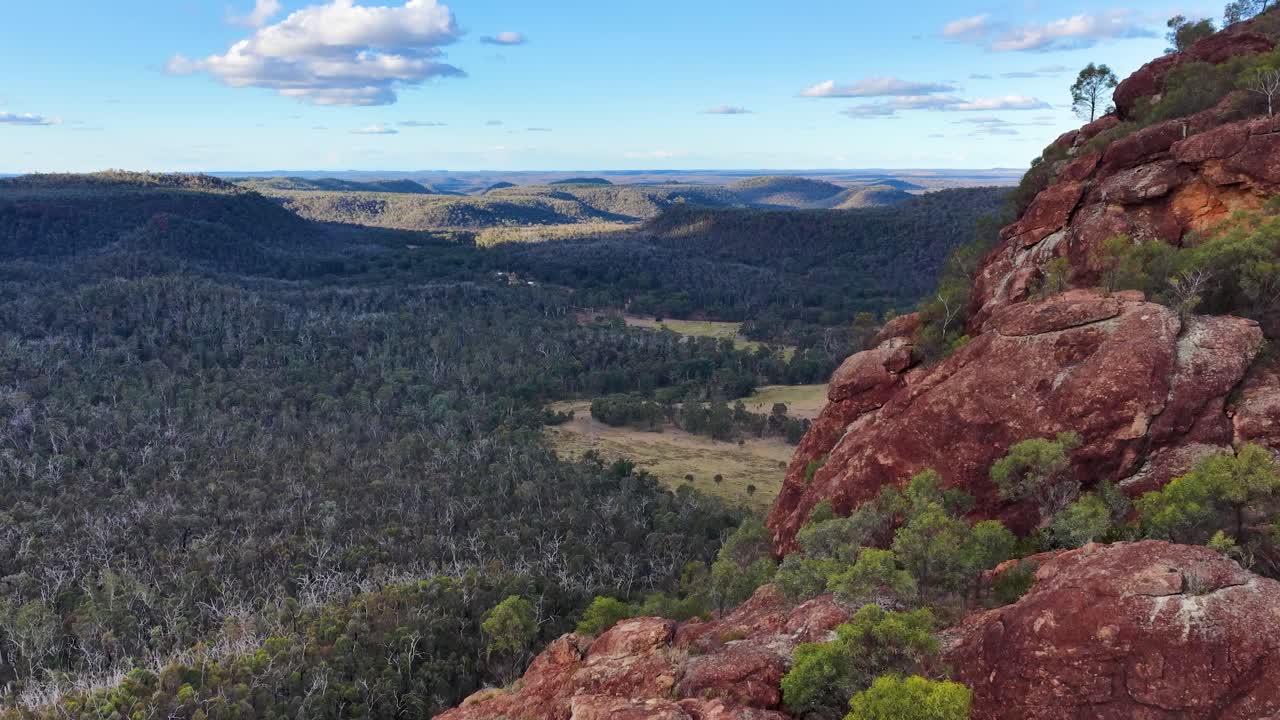 Drone pans from volcanic outcrop to vast forest landscape, warm sunset lighting, wide aerial view