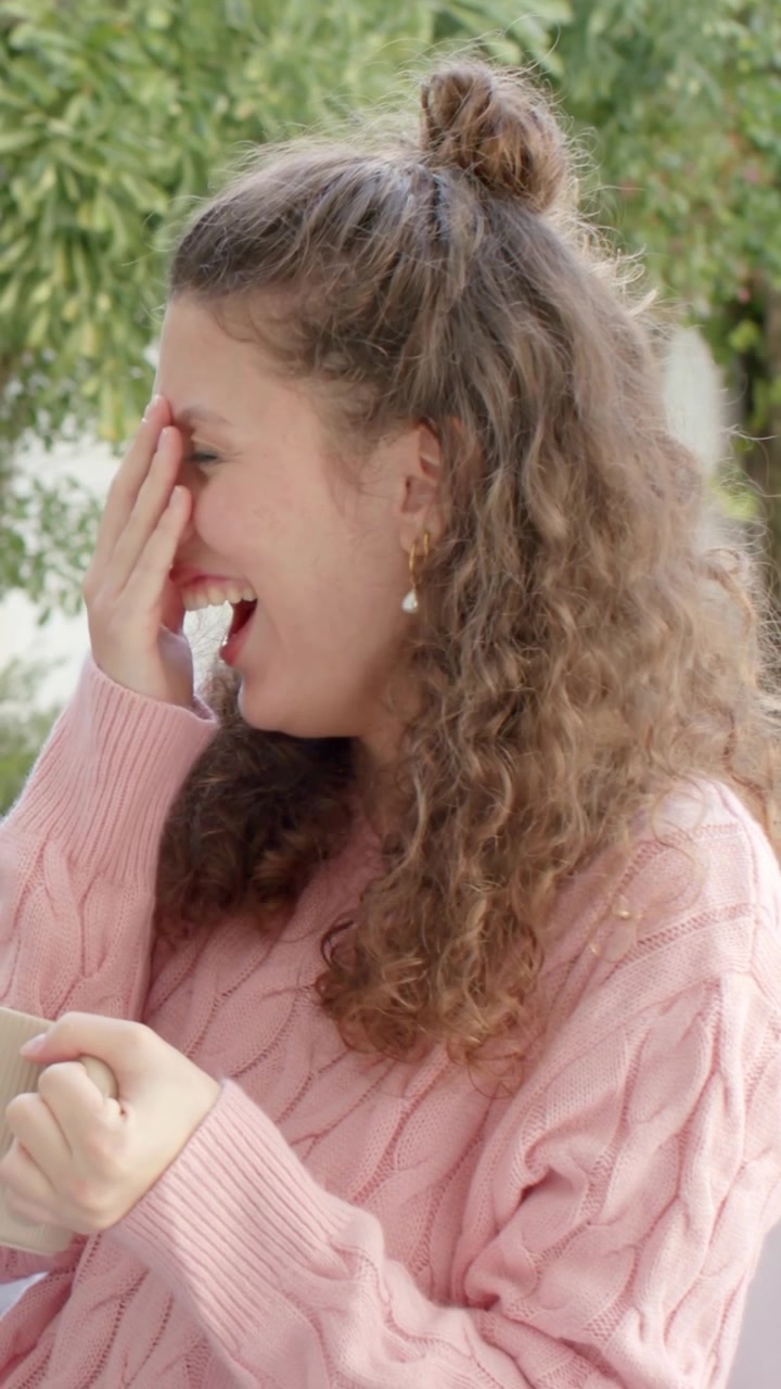 Donna che ride e si copre il viso in terrazza dopo una battuta fuori campo, con cuori a tema marketing che fluttuano intorno.