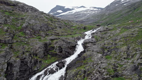 aerial shot, tracking up from the top of the large stigfossen waterfall to reveal a large snow capped mountains and a wide valley in the distance