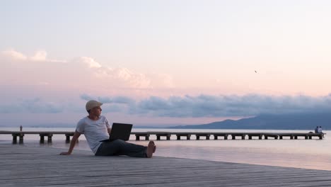male traveler sitting on the shore using laptop. digital nomad or remote worker concept