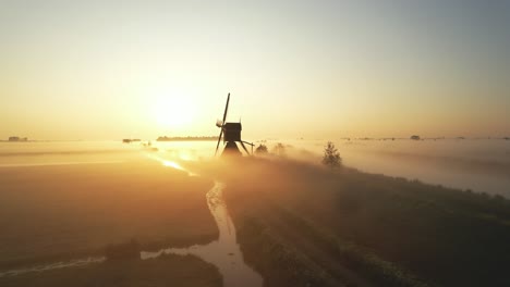 drone shot flying backwards rising up reveiling a dutch windmill with a misty morning sunrise in the background in 4k