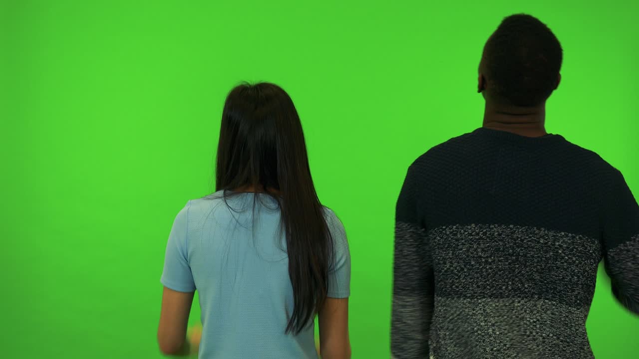 Uma mulher asiática e uma mulher negra torcem de costas para a câmera - estúdio com tela verde.