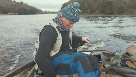 Mature-man-bailing-lake-boat-while-driving-outboard-engine