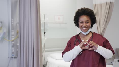 Portrait-of-happy-african-american-female-doctor-with-face-mask-in-hospital-room,-slow-motion