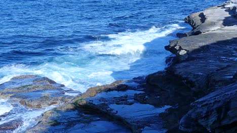 scenery of crashing waves against rocky coastal hills during sunny day