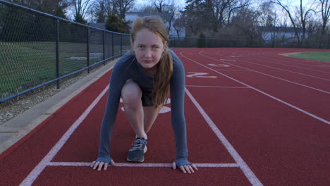 a teen girl in the ready position on a running track