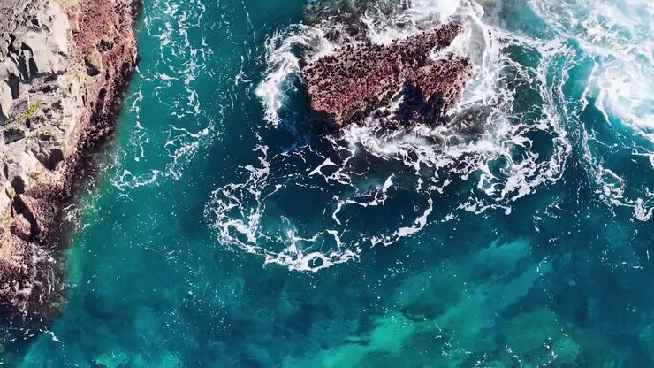 Top-down drone-opname van turkoois water en wit zeeschuim dat tegen rotsen slaat in Australië.