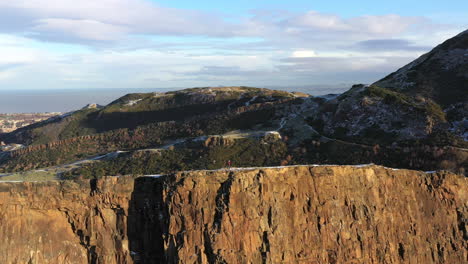 Aerial-shot-of-a-tourist-looking-out-on-Edinburgh-standing-on-Salisbury-crags-on-a-beautiful-summers-day