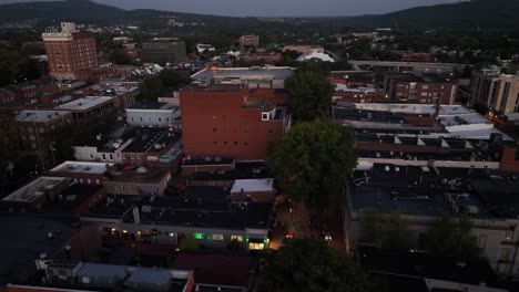 historic american town at dusk with lighting paramount theater in downtown. rising drone wide shot. housing area with tower and block in center of small town. rooftops of houses and air conditioner.