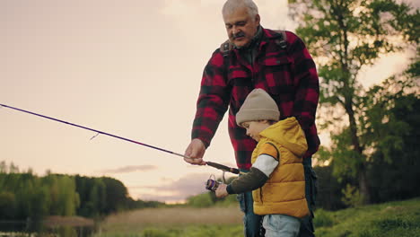 il ragazzo sta pescando nel lago il nonno o il padre lo stanno aiutando la famiglia felice si sta riposando in natura