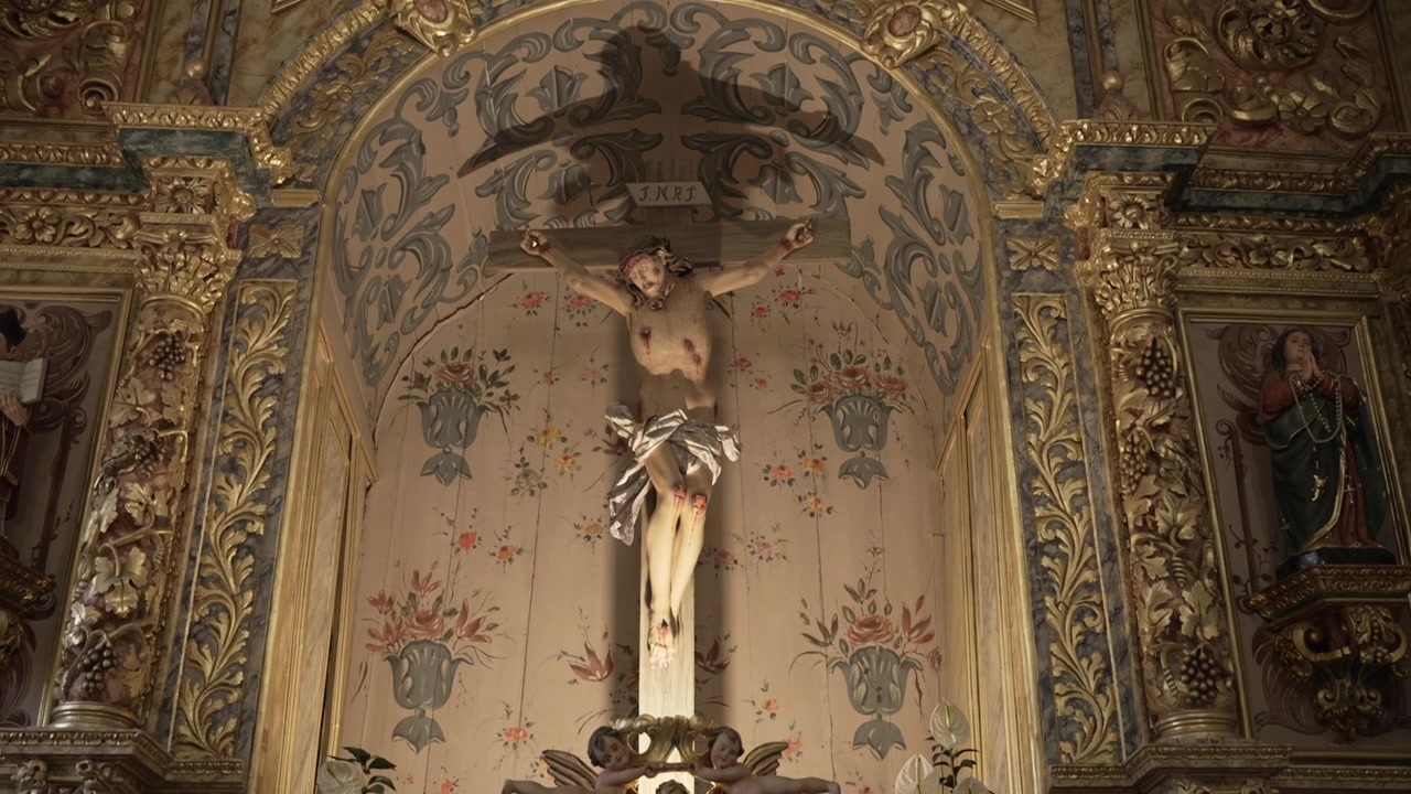 Detailní pohled na krucifix na bohatě zdobeném kostelním oltáři s květinovými a zlatými akcenty.