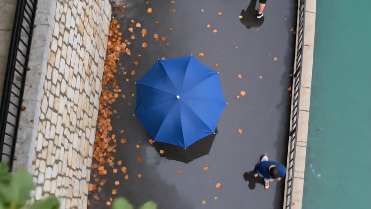 Pedoni che entrano dall'alto, camminando lungo un sentiero lungo il fiume oltre un ombrello blu aperto, proseguendo.