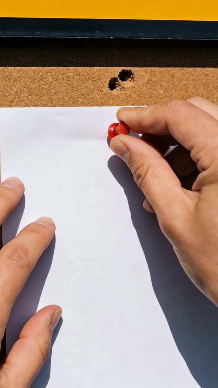 Vertical video: Holding white sheet, hands pushing red push pin into corkboard, securing paper