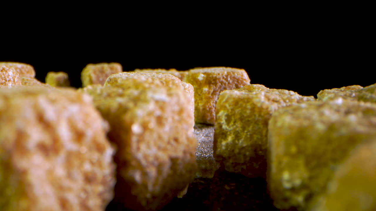 foto macro de trozos de azúcar moreno cayendo sobre una superficie de espejo negro