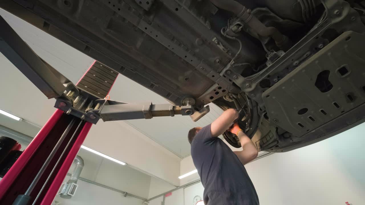 joven mecánico profesional que trabaja bajo el coche moderno levantado en el servicio de reparación de automóviles. servicio de automóviles, mantenimiento de reparación.