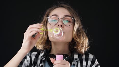 retrato en primer plano de una chica feliz y emocional soplando una gran burbuja de jabón con un palo en un fondo negro. imágenes de estudio de una morena con cabello corto y labios sensuales con auriculares en el cuello