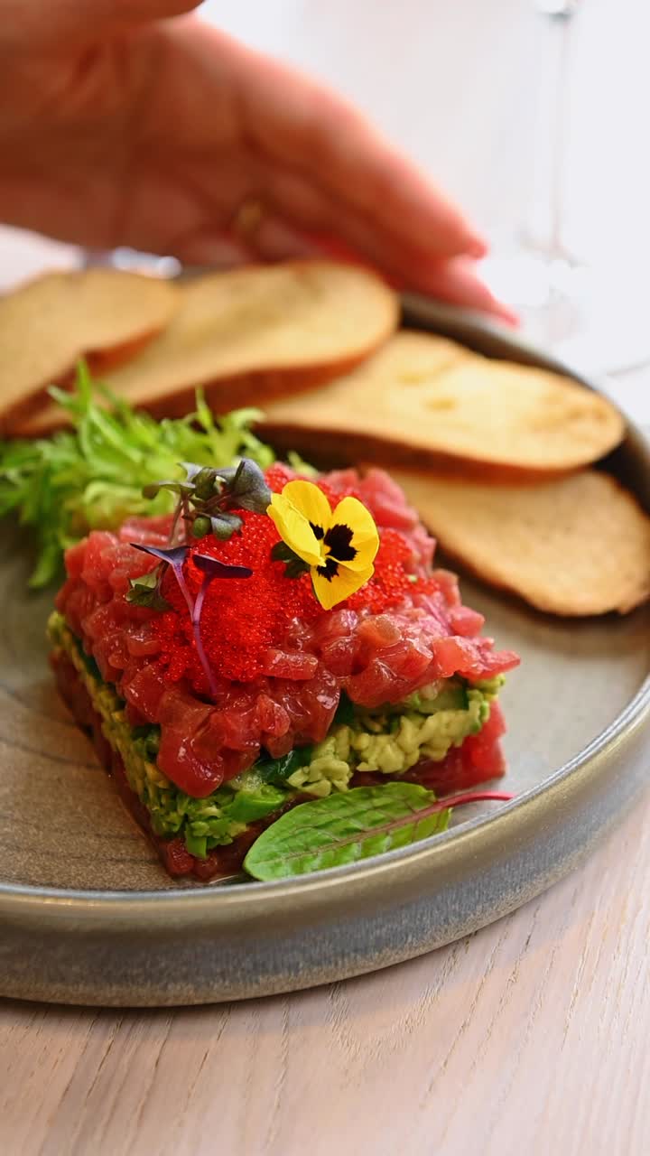 Tuna tartare with avocado and red caviar on plate. Gourmet tuna tartare with avocado layers, red fish roe, microgreens, and toasted bread on a gray ceramic plate