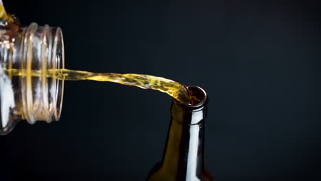 Vertical-Shot-Of-Beer-Pouring-From-Glass-Bottle-In-Plain-Background