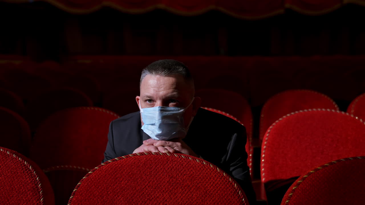 Spectator in medical mask sitting alone in theater. One man in protective mask watching a play in empty auditorium during coronavirus.