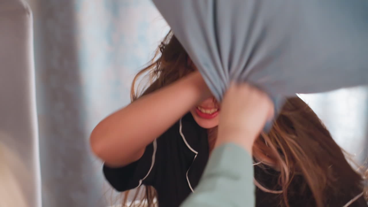 Close up of playful kids joyfully engaged in pillow fight, one child blocks incoming pillow with arm while laughing, creating dynamic moment filled with movement