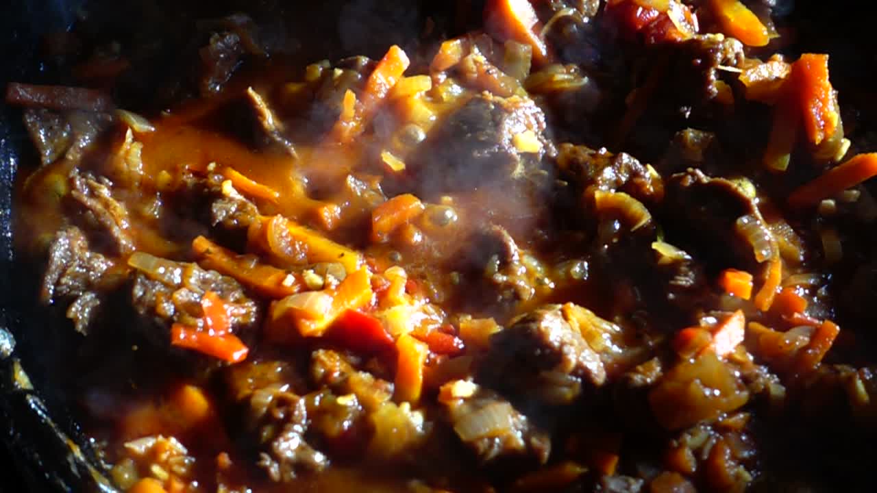 Proses persiapan goulash dengan sayuran dalam wajan besi cor. Gerak lambat
