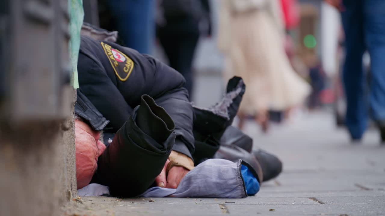 Close-up of a homeless old man sleeping on the pavement wrapped in a black jacket with blurred street on the background in London, England