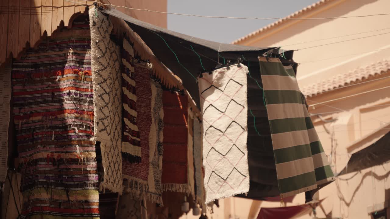 Handwoven Moroccan rugs of different patterns hang outside a market stall in sunlight