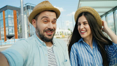 vista de cerca de una joven y feliz pareja caucásica de turistas con sombreros hablando, agitando las manos y sonriendo a la cámara al aire libre en verano